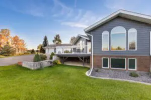 A two-story gray house with a wooden deck and a winding grass path leading to the entrancev
