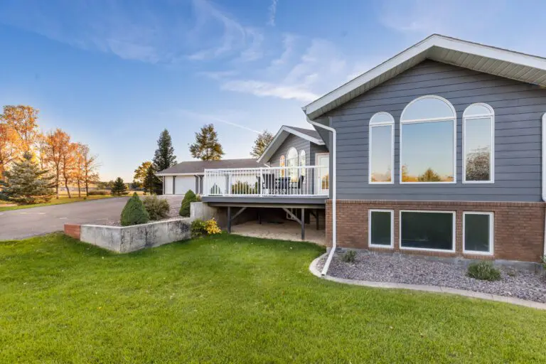 A two-story gray house with a wooden deck and a winding grass path leading to the entrancev